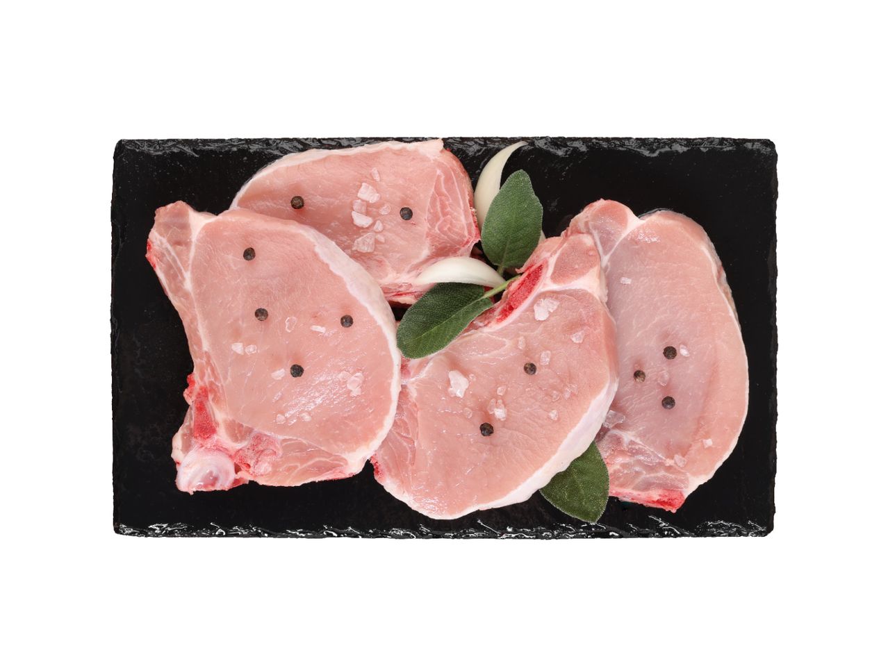 Sveži svinjski kotleti sa začinima na crnoj ploči.