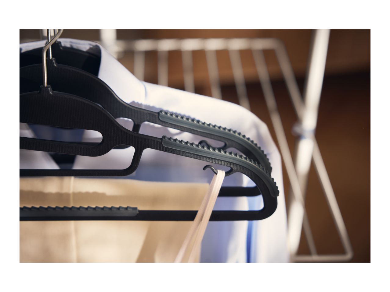 Black clothes hangers with shirts and trousers hanging on a drying rack.