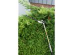 An extendable hedge trimmer in front of a green hedge.