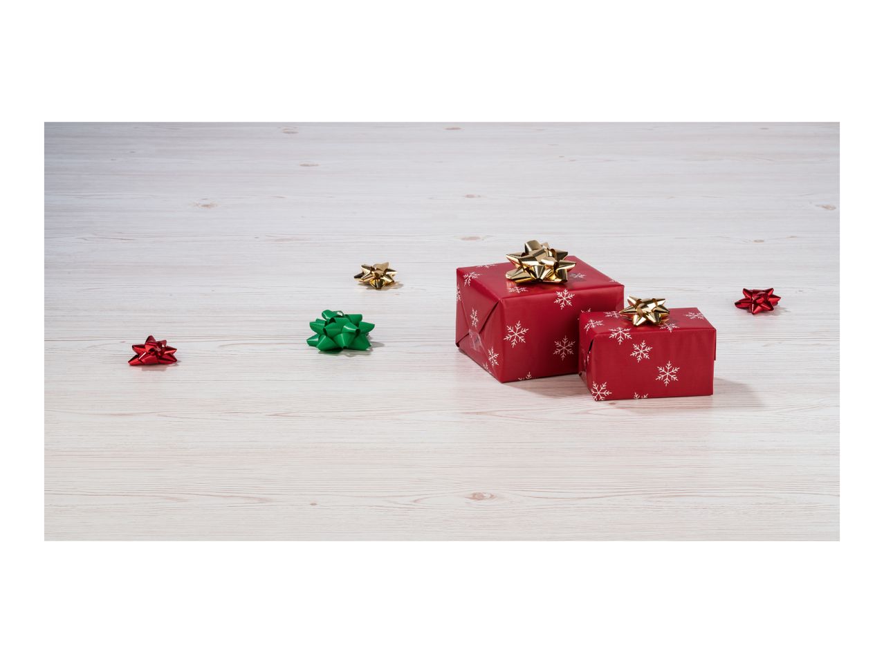 Two red gift boxes with gold bows and scattered decorative bows on a wooden surface.