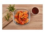 Marinated chicken wings in a glass dish with rosemary and a bowl of sauce on a wooden table.