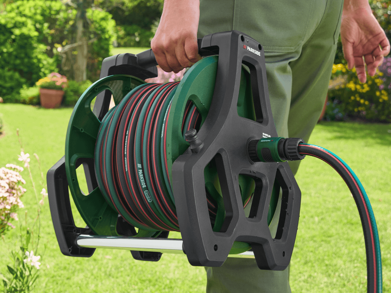 Gartenschlauch auf einer Schlauchtrommel, von einer Person im Garten getragen.