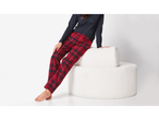 Esmara: Femeie în pantaloni de pijama în carouri roșii și negre, așezată pe un puf alb.