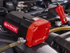 An Ultimate Speed oil extractor pump connected to a car engine with battery clamps.