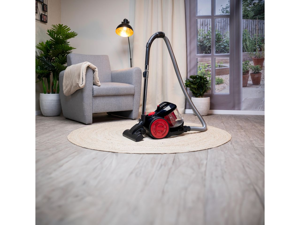 A red and black upright vacuum cleaner sits on a rug in a living room.