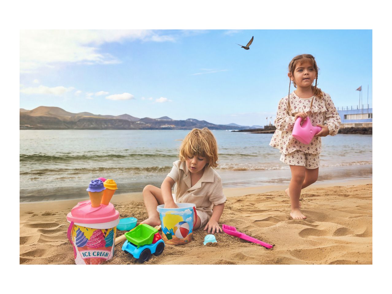 Two children playing with beach toys, including buckets, a truck, and a watering can.