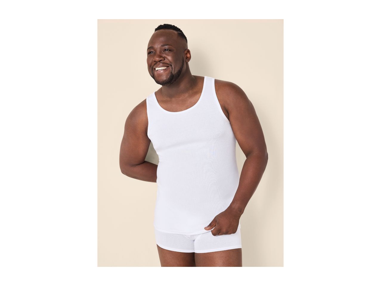 A smiling man wearing a white tank top and matching boxer shorts.