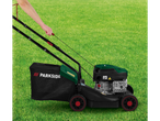 A person pulls the starter cord of a Parkside lawnmower on a grassy lawn.