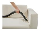Hand vacuuming dirt from a white sofa with a crevice tool attachment.