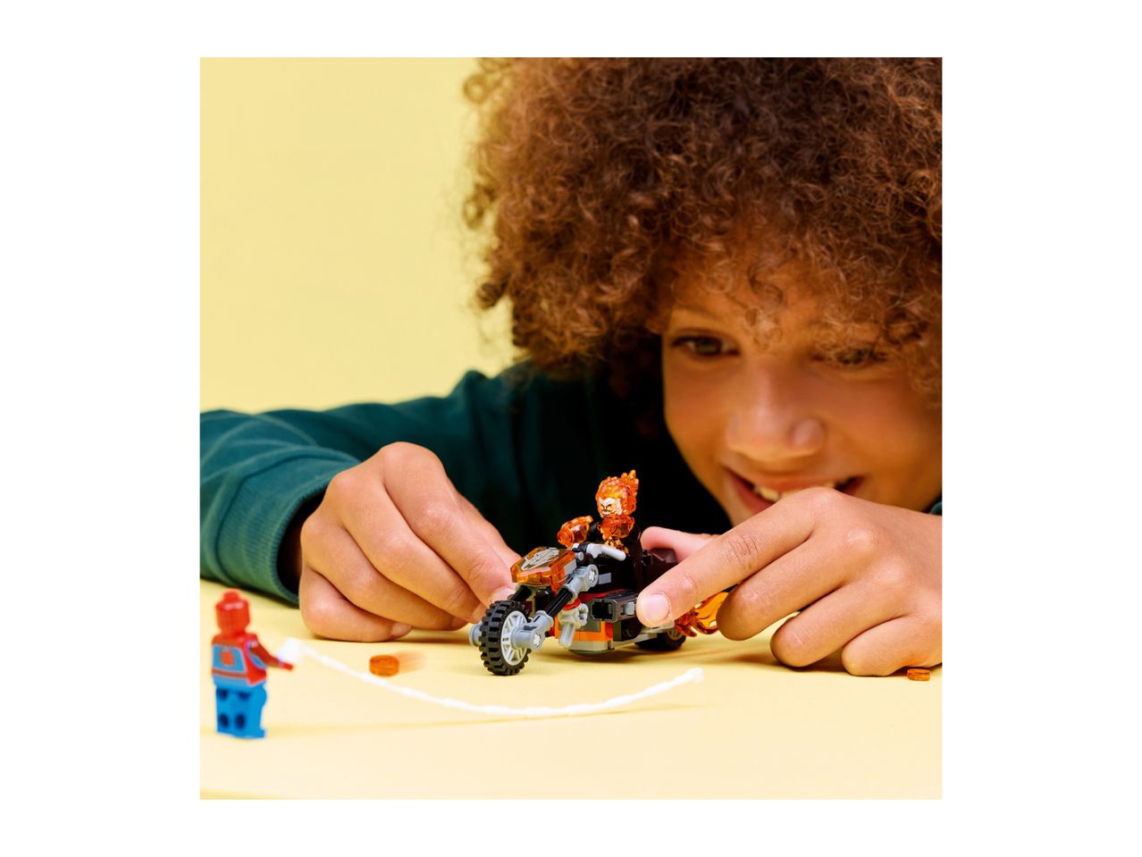 A child playing with a toy motorcycle and a superhero figurine on a yellow surface.