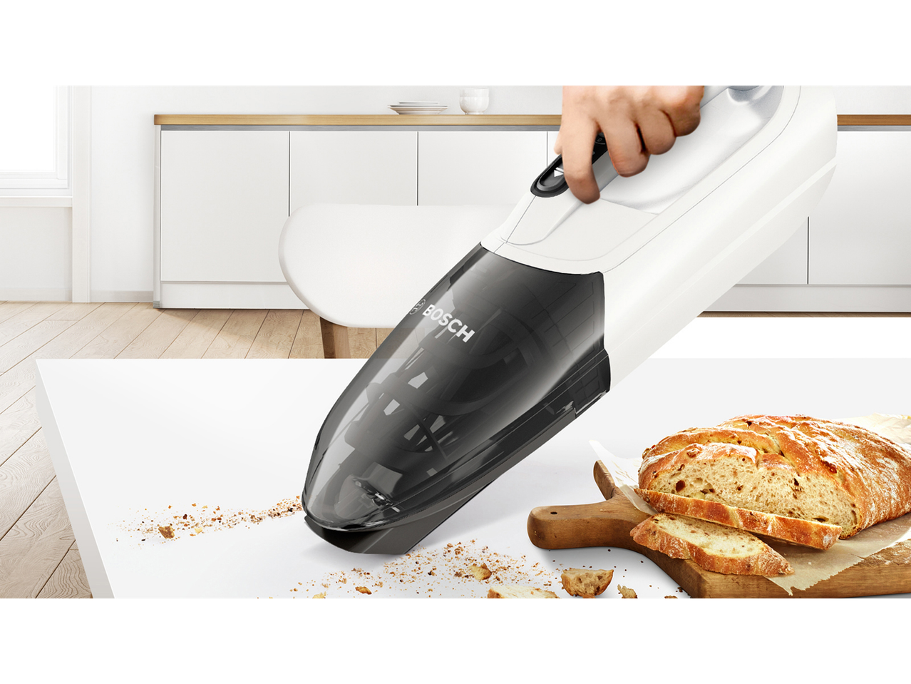 Ročni sesalnik Bosch sesa drobtine kruha na kuhinjskem pultu.