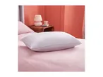 A white pillow with grey trim on a pink bed with a lamp and mug on a nightstand.