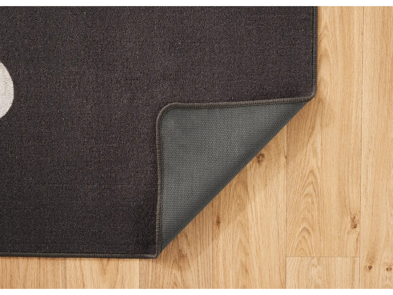 Dark gray LIVARNO home rug with a lifted corner on a wooden floor.