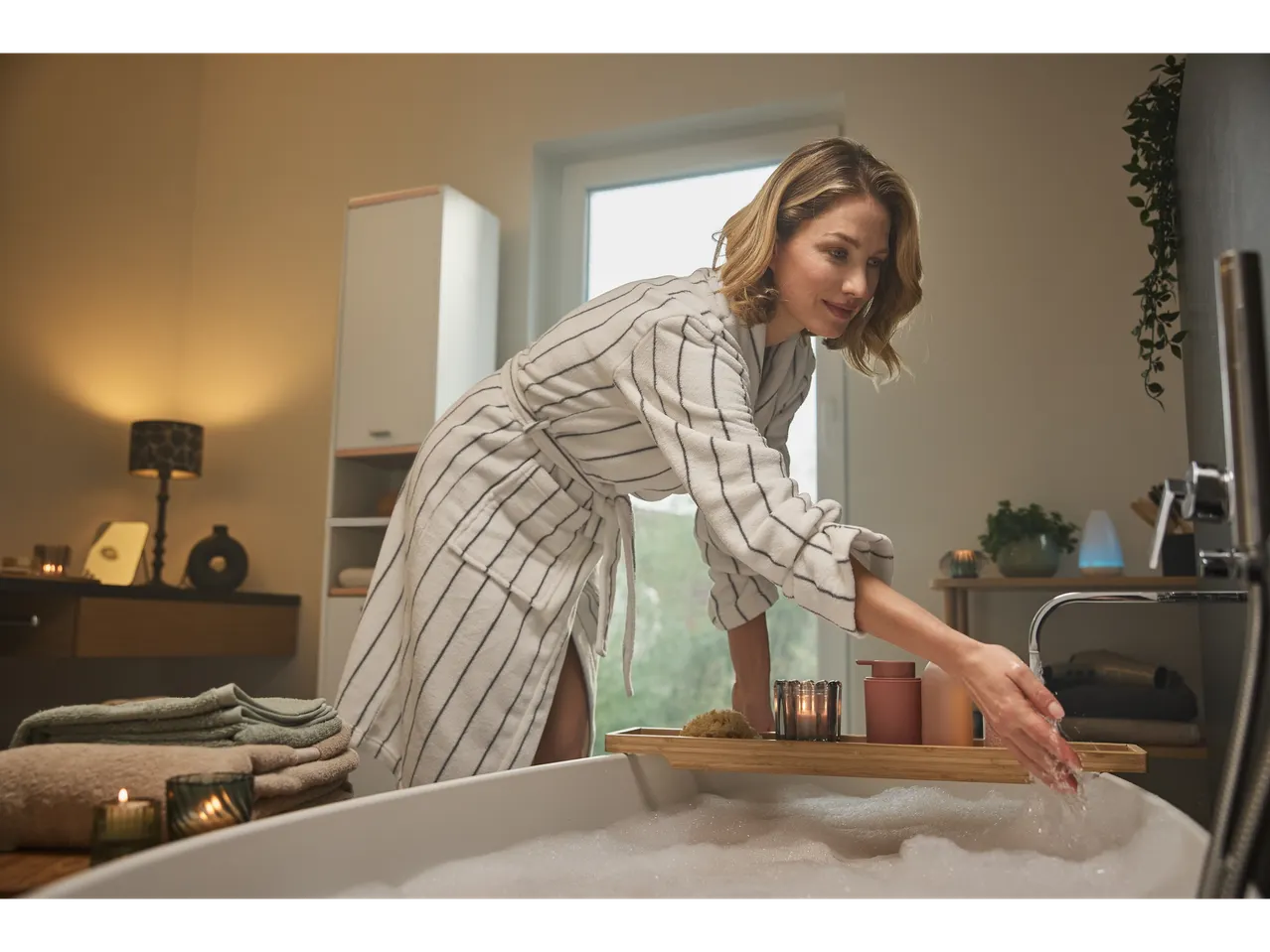 A woman in a robe fills a bubble bath with warm water.