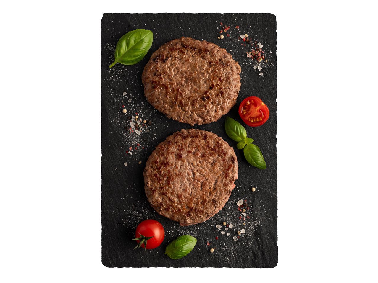 Két grillezett hamburgerpogácsa bazsalikommal és koktélparadicsommal.
