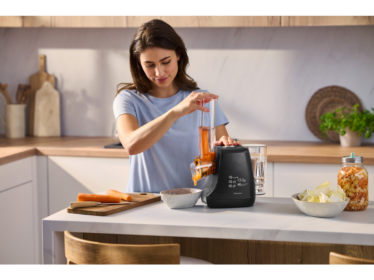 Mulher na cozinha usando um ralador elétrico de vegetais SILVERCREST para ralar cenouras.