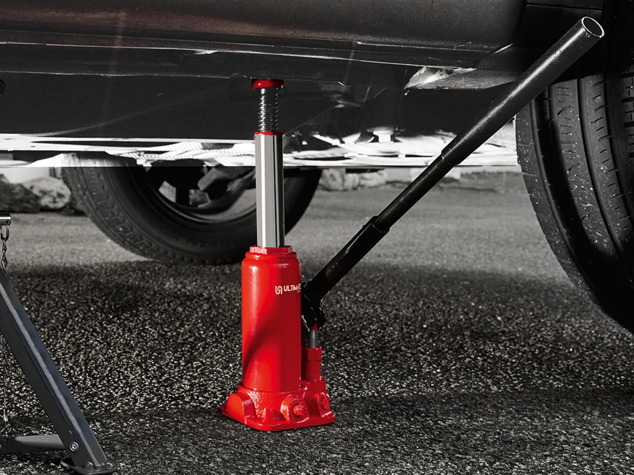 Rdeča hidravlična dvigalka pod avtomobilom, pripravljena za dvig.