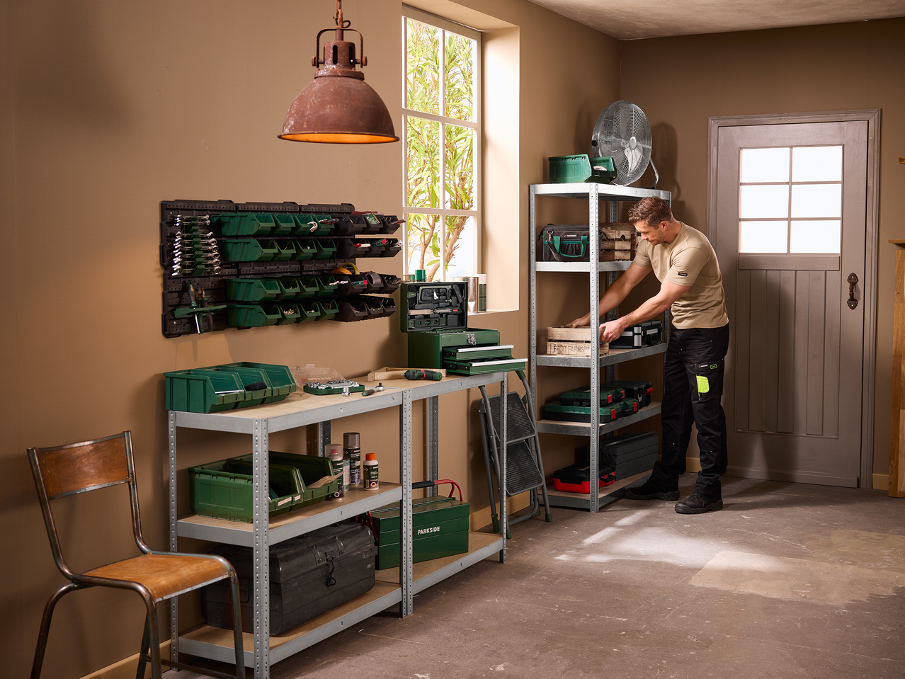Άνδρας οργανώνει ένα εργαστήριο γκαράζ με μεταλλικά ράφια, κάδους αποθήκευσης και εργαλειοθήκες.