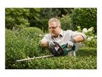 A man in safety glasses and gloves trimming a green hedge with a cordless hedge trimmer.