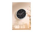 A black and white wall clock with temperature and humidity gauges, next to a vase with flowers.
