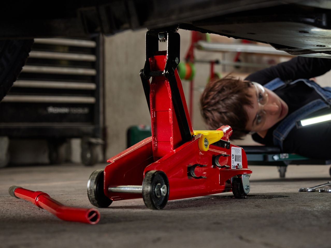 A red car jack lifting a vehicle, with a person working underneath.