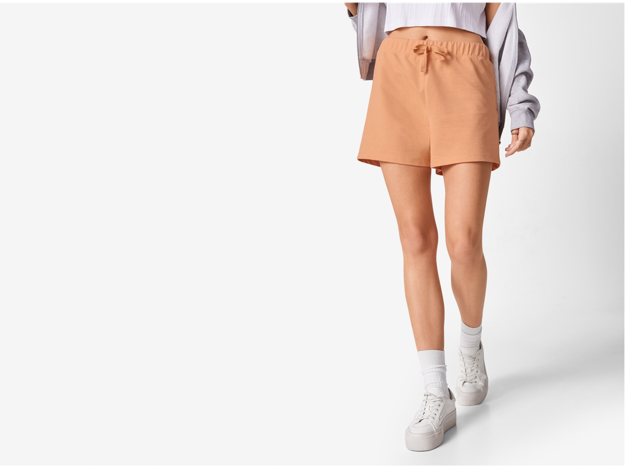 Femeie purtând pantaloni scurți piersici și adidași albi.