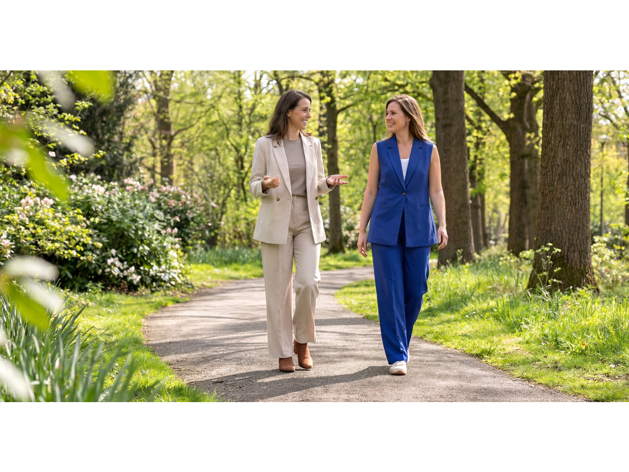 Duas mulheres com blazers ESMARA, um bege e um azul, a caminhar num parque.