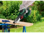 Cordless chainsaw cutting a wooden board in a garden.