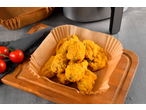 Nuggets de frango em forma de papel sobre uma tábua de madeira com tomates e uma fritadeira de ar.