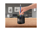 A hand inserts a blue pencil into a black electric pencil sharpener on a wooden table.