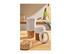 Two storage containers with cereal and cocoa powder, and a bowl of cereal on a wooden counter.