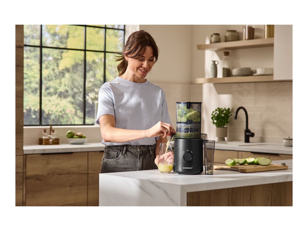 Woman making green juice with a juicer in a modern kitchen.