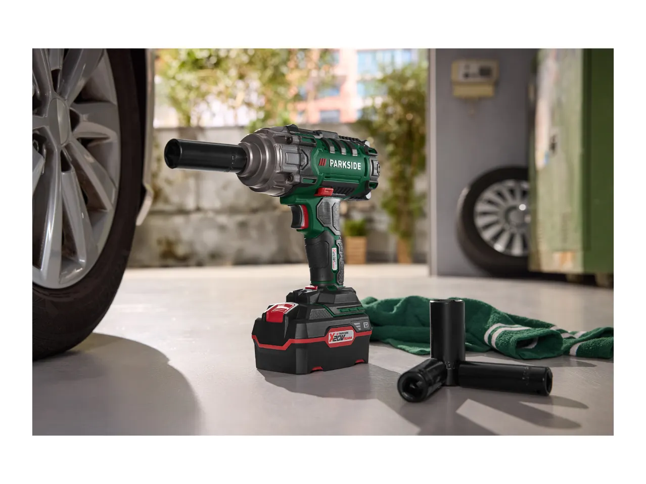 Cordless impact wrench with battery pack, sockets and a car wheel in the background.
