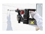A person using a cordless rotary hammer drill to make a hole in a white brick wall.