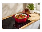 A red cast iron pot filled with vegetables on a black induction cooktop.