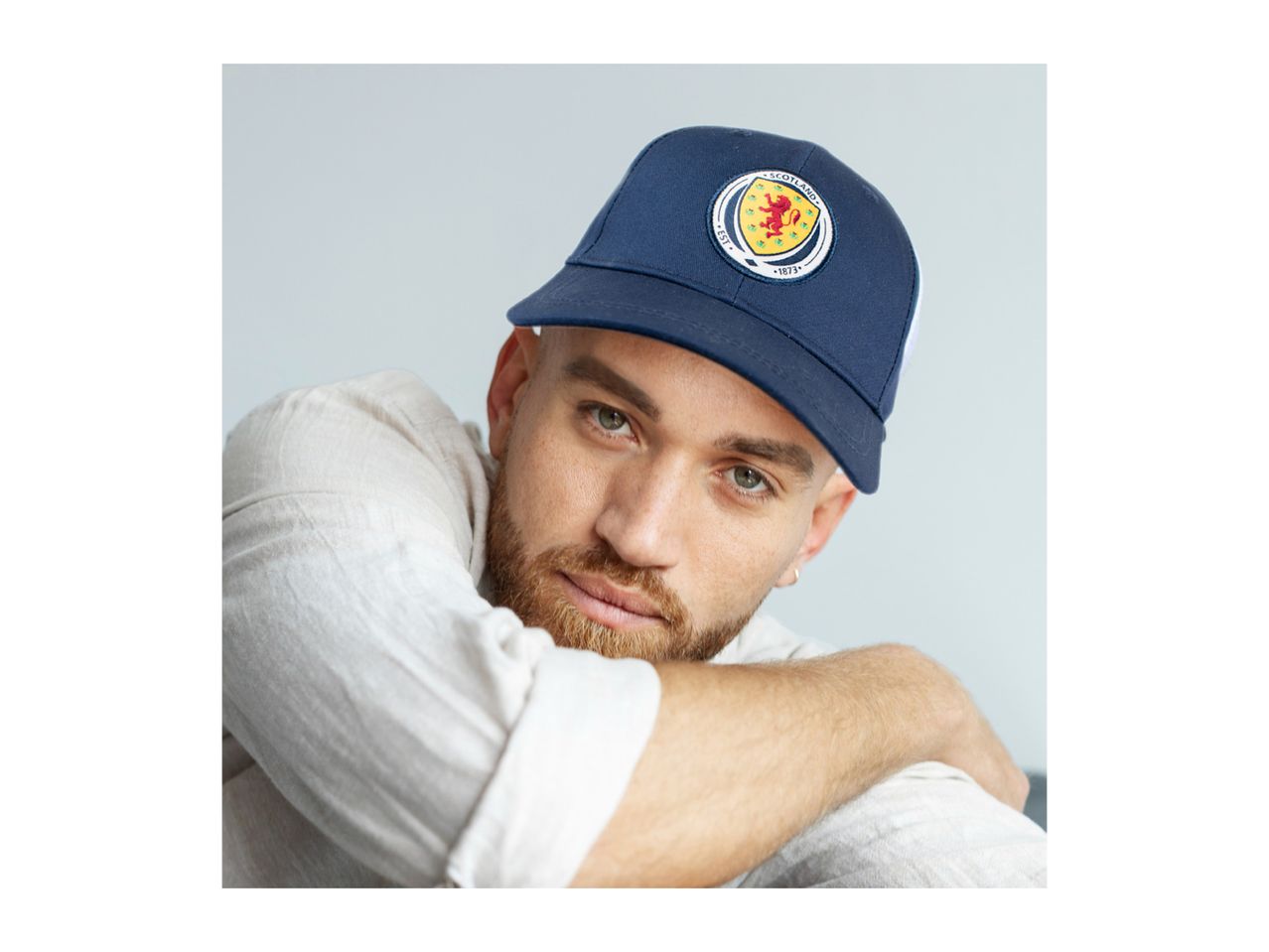 Man wearing a navy blue baseball cap with a circular Scotland crest, light shirt.
