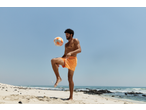 Man in orange CRIVIT shorts playing with a Neoprene Ball on a sunny beach.