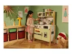 Child playing with a toy kitchen, decorated for Christmas with an 'XMAS' sign.