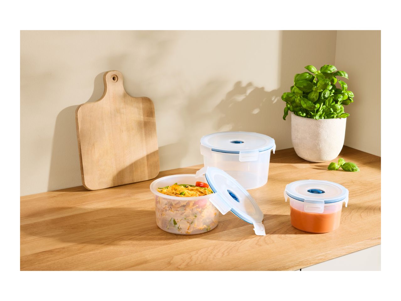 Three round plastic food storage containers on a wooden kitchen countertop.