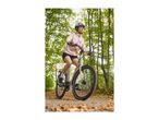 Woman in a pink jacket and helmet riding a bicycle on a path with autumn leaves.