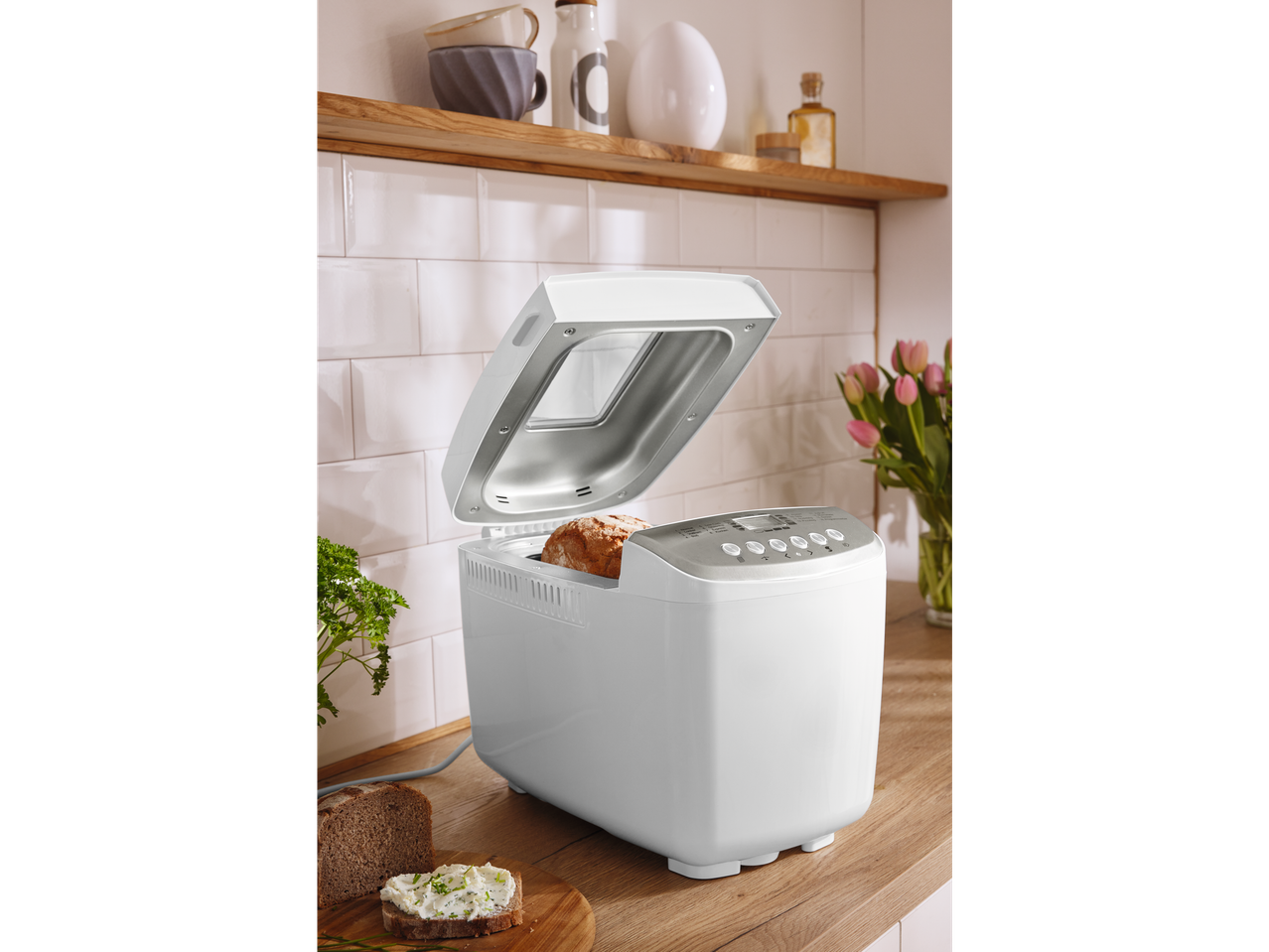 Machine à pain blanche avec couvercle ouvert sur un comptoir de cuisine avec du pain frais et des tartines.
