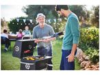 Deux hommes cuisinent sur un barbecue Weber dans un jardin.