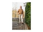 Elderly man walking with a cane on a paved path next to a green hedge.
