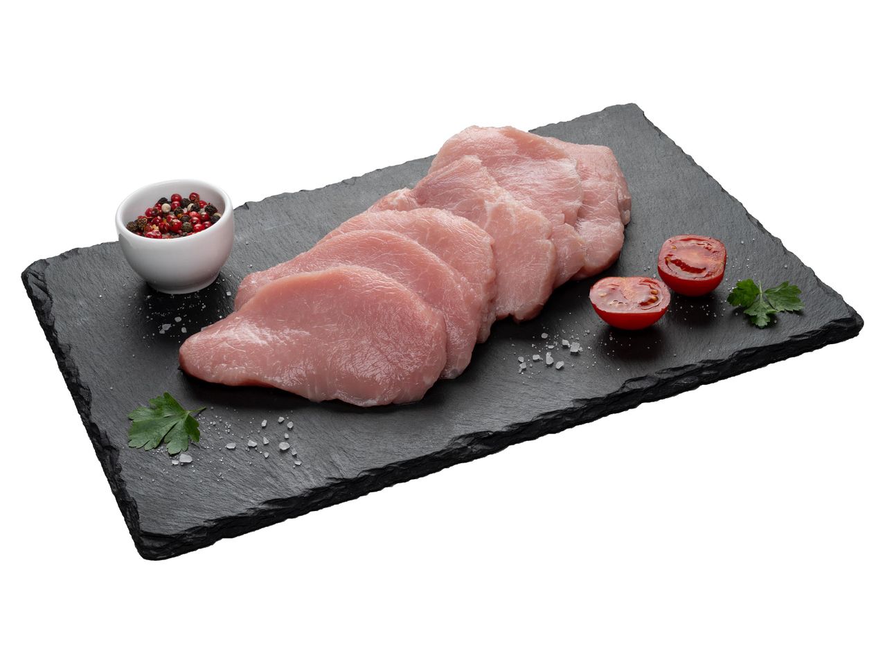 Nyers pulykamell szeletek, bors és paradicsom fekete palatáblán.