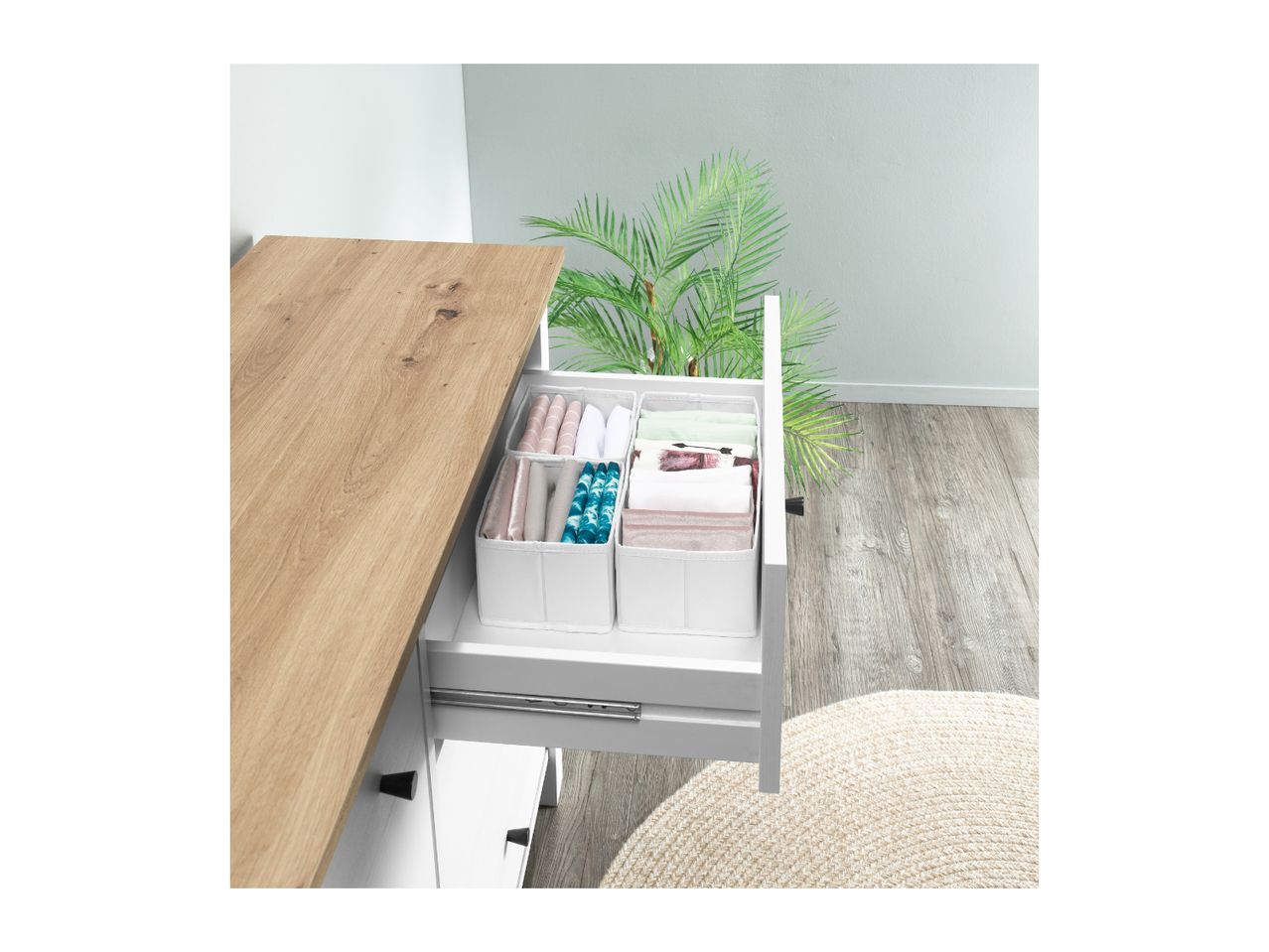 Open drawer with white fabric organizers holding folded clothes, next to a plant.