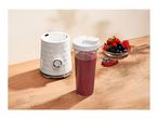 A white personal blender base next to a cup filled with berry smoothie and fresh berries.