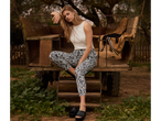Žena modelira šarene pantalone, beli top i crne papuče na rustikalnom vozu.