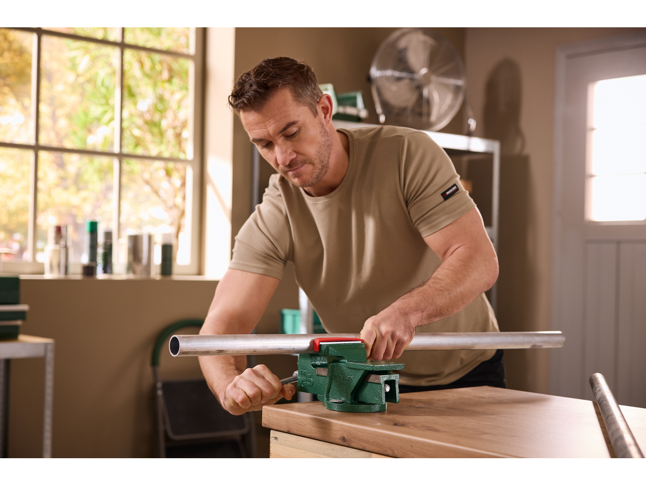 Άνδρας χρησιμοποιεί μέγγενη PARKSIDE® για να επεξεργαστεί έναν μεταλλικό σωλήνα σε ξύλινο τραπέζι.