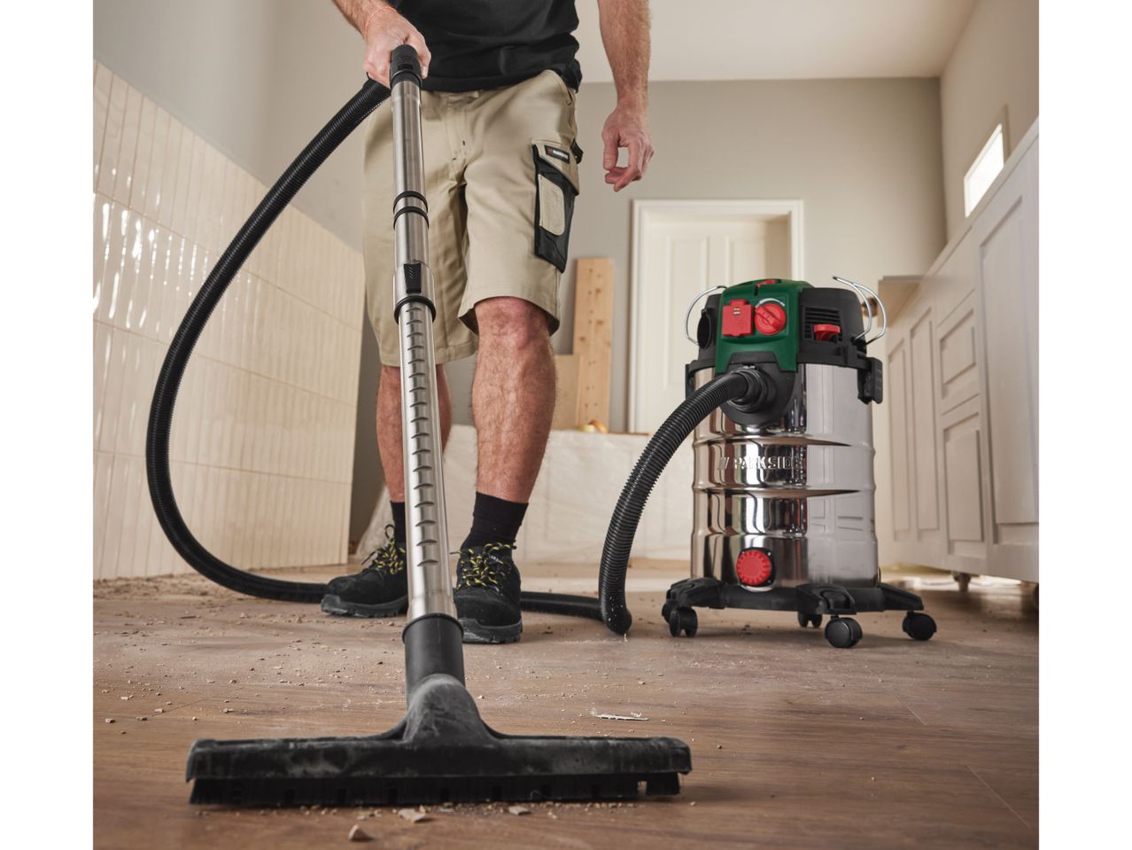 A person uses a Bosch wet/dry vacuum cleaner to clean up sawdust on a floor.