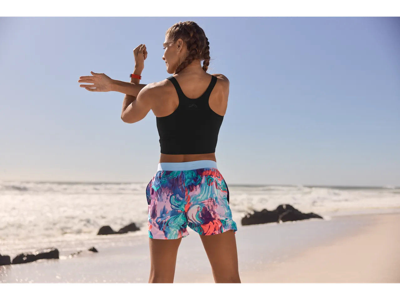 Femeie în sutien sport și pantaloni scurți cu flori se întinde pe plajă.